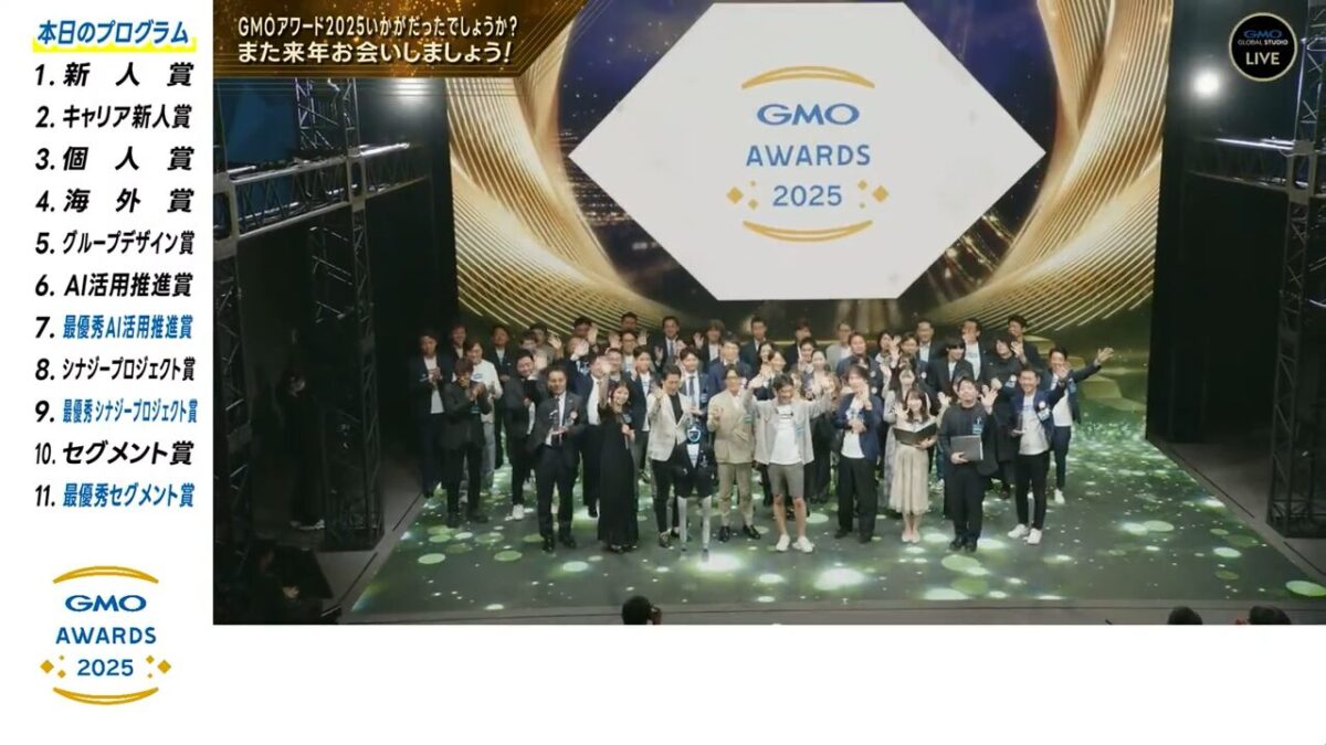 GMOインターネットグループの年間表彰式「GMOアワード2025」の終演風景。新人賞、AI活用推進賞、シナジープロジェクト賞、セグメント賞など、全11の表彰カテゴリを網羅したプログラム一覧が左側に表示されている。ステージ上の出演者全員が笑顔で手を振る、華やかなイベントの締めくくり。